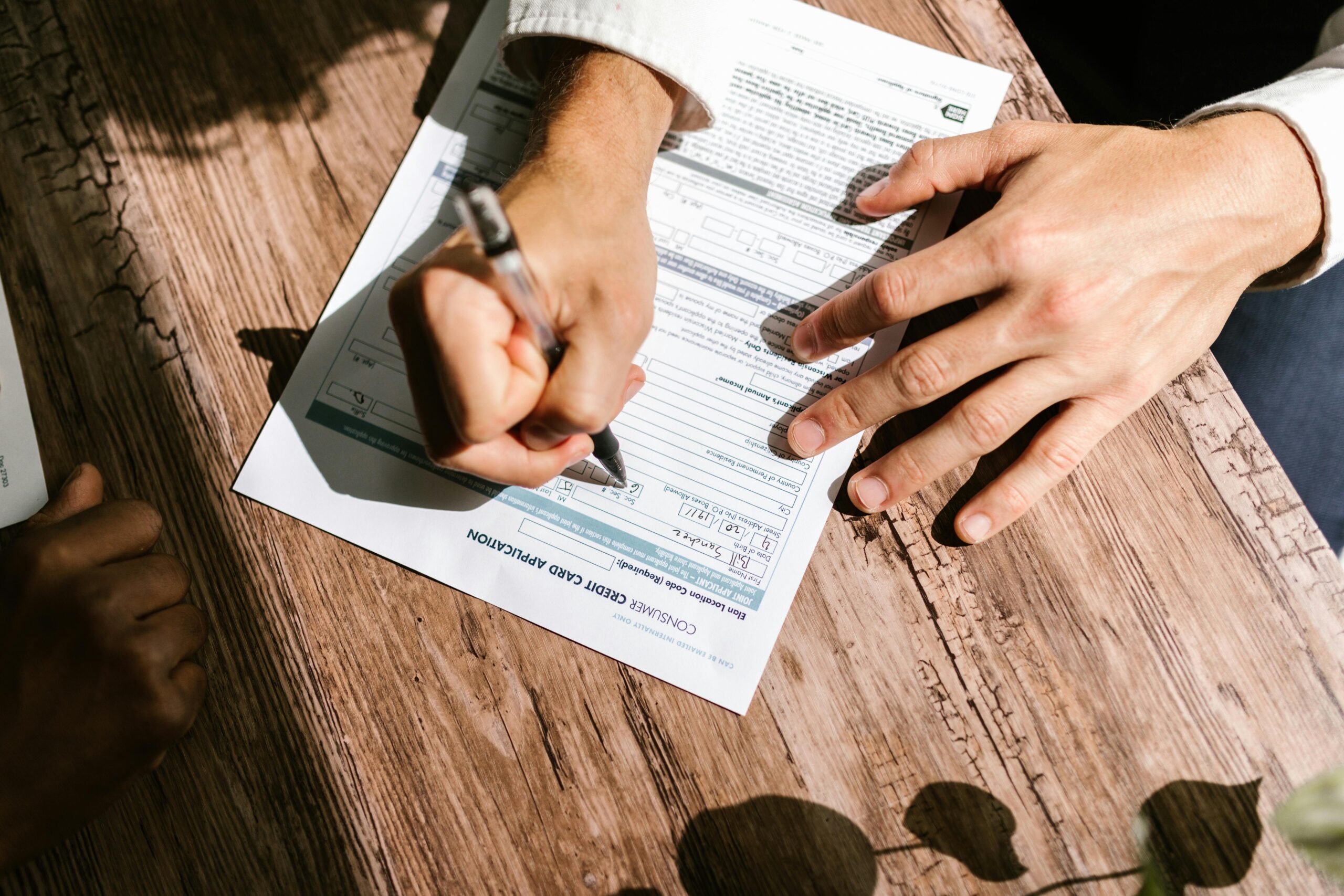 pexels-photo-7821513-7821513 Hands writing on a consumer loan credit application form on a wooden table.